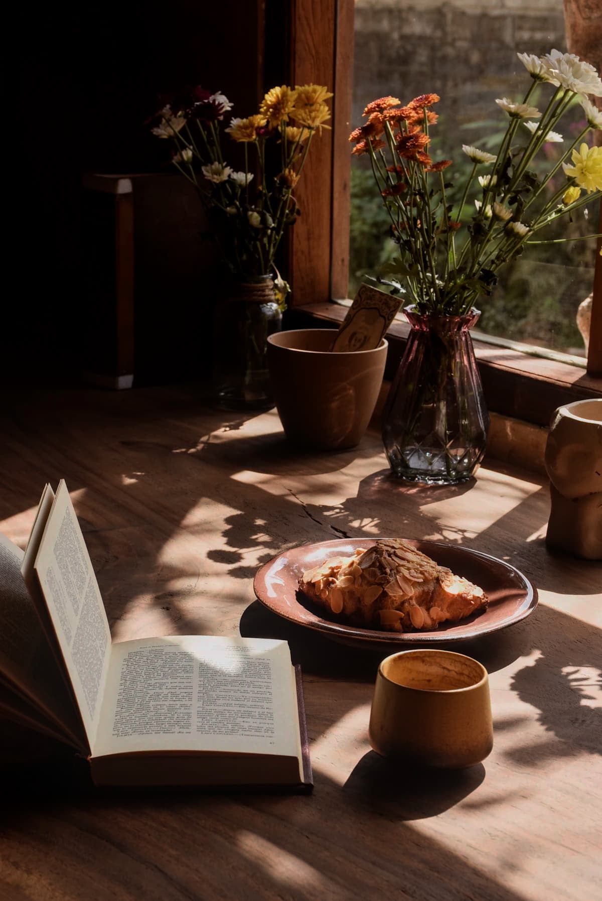 An open book, croissant and coffee by a sunlit window